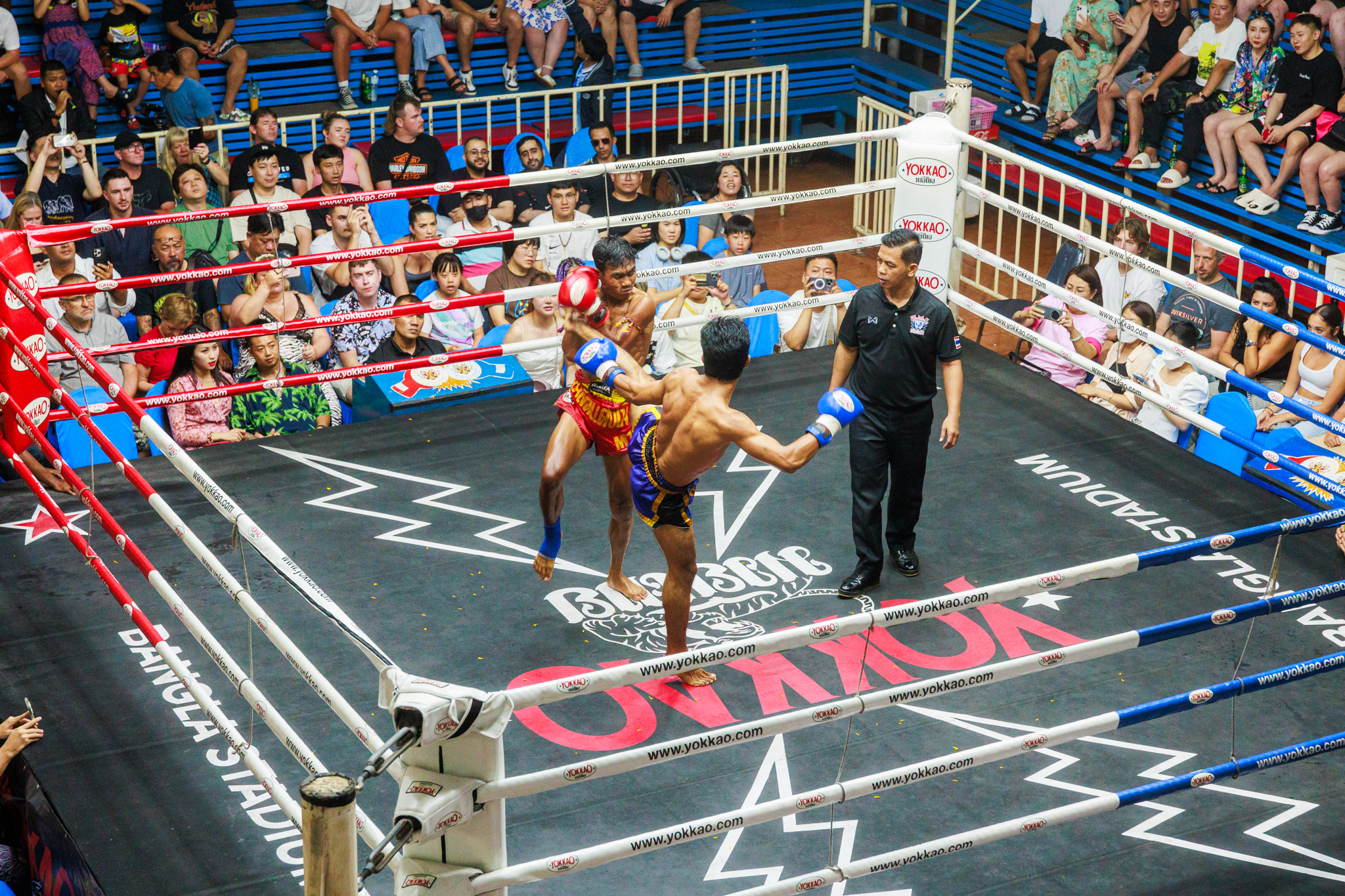 The blue Muay Thai boxer is kicking, the red Muay Thai boxer is defending