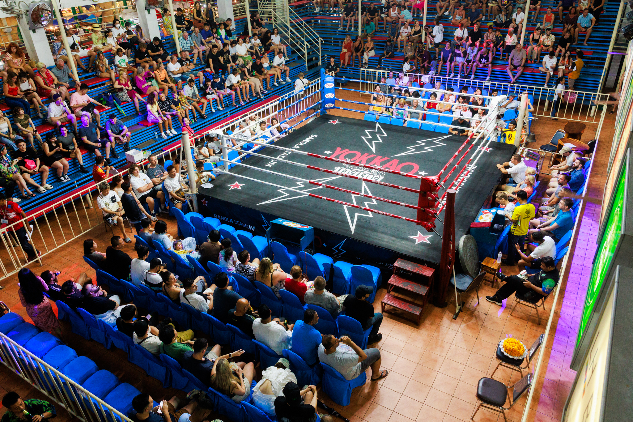 Bangla Stadium - A boxing ring in a large indoor arena with spectators watching the intense match.