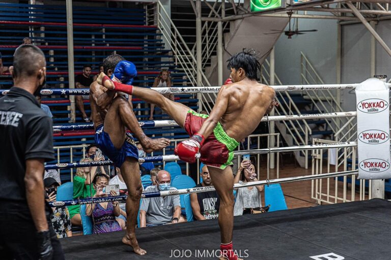 Two men in boxing attire exchanging kicks in the ring during a competitive match.