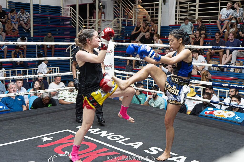 Two women wearing boxing gear, engaged in a match inside a boxing ring.