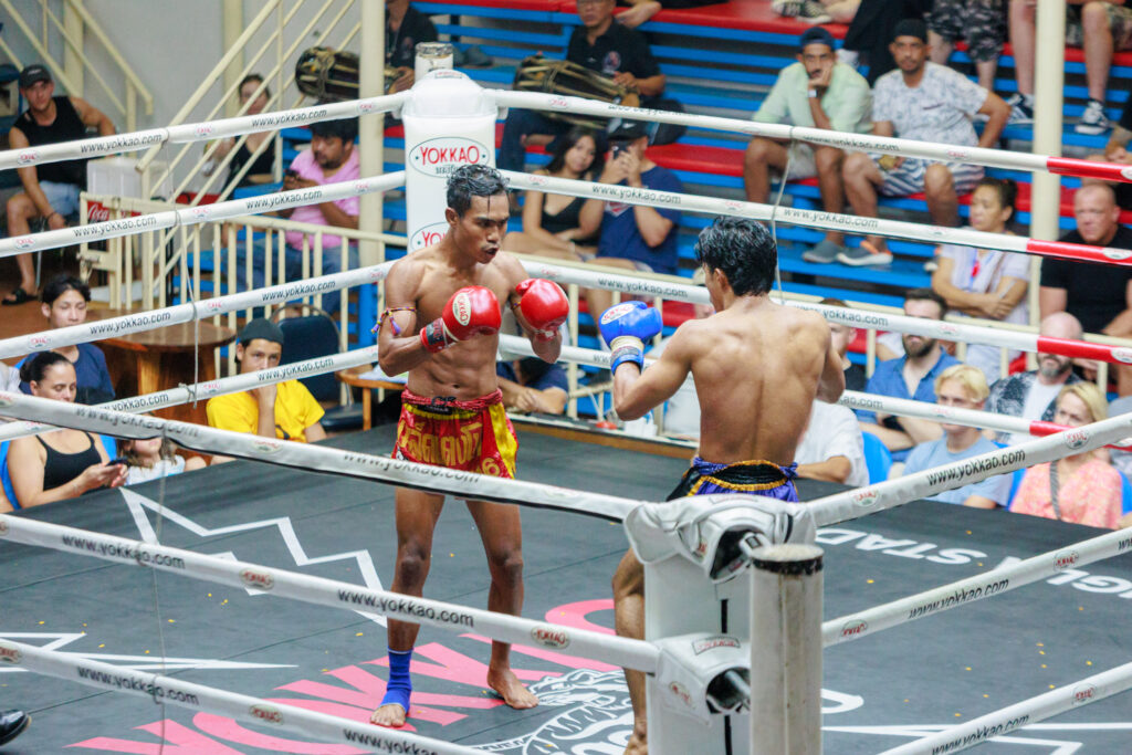 Two Muay Thai boxers fighting in a ring, surrounded by spectators watching the intense match.