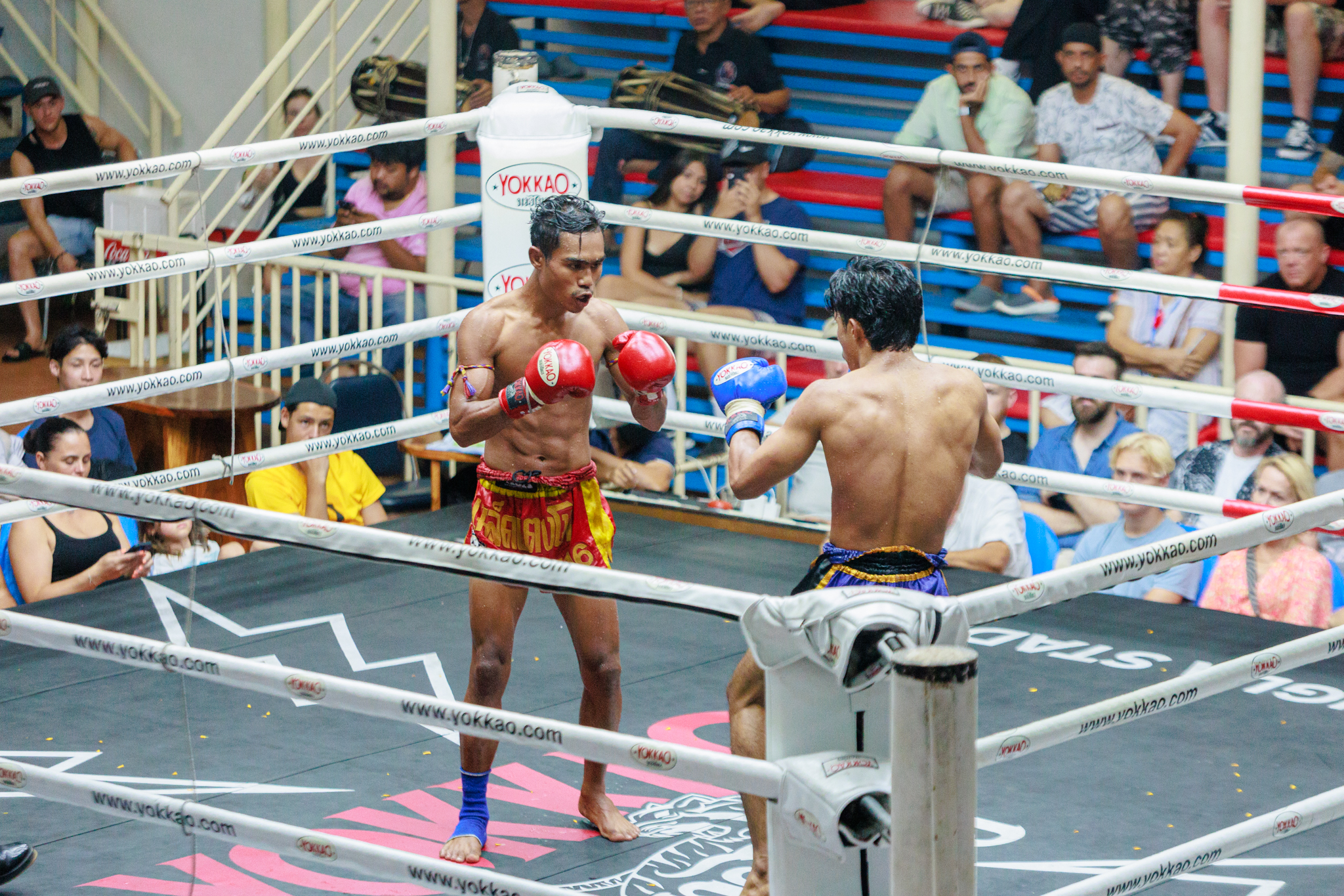 Two Muay Thai boxers fighting in a ring, surrounded by spectators watching the intense match.