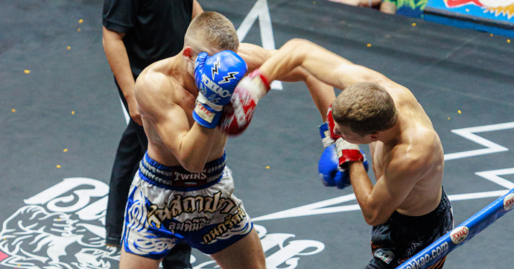 Two Muay Thai fighters in boxing gear engaged in a ground fight