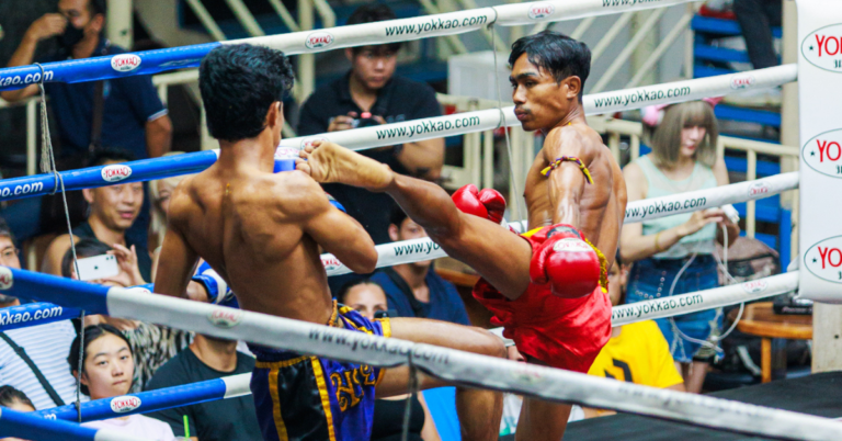 Two Muay Thai fighters in a boxing ring, one delivering a powerful kick to the other.