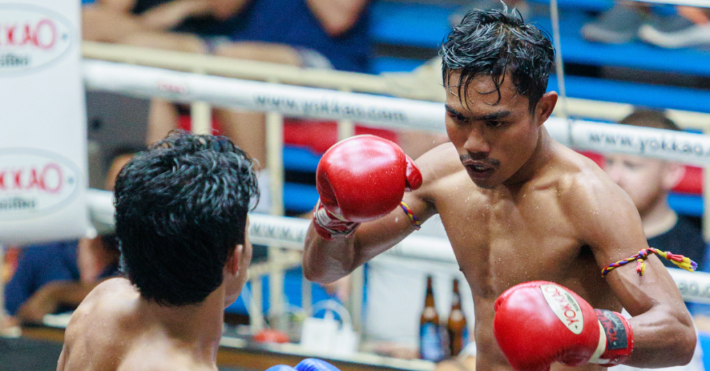 Two Muay Thai boxers in a ring, one wearing red gloves