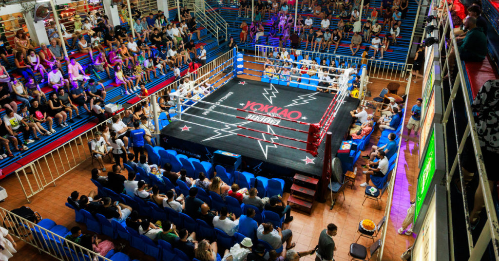 A boxing ring set in a spacious arena, with a crowd of spectators eagerly watching a live Muay Thai competition