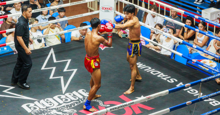 Two men engage in a Muay Thai match in a boxing ring, with spectators attentively watching the intense competition