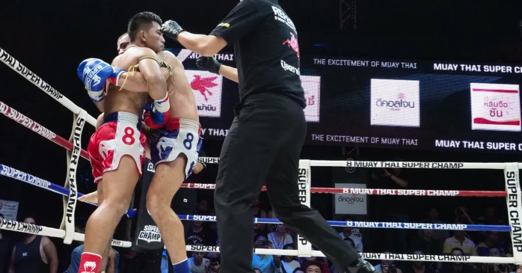 In the ring, a Muay Thai boxer executes a knee strike