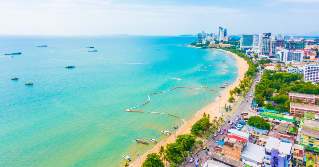 A scenic view of Patong Beach during the day, featuring clear blue waters, golden sands, and surrounding urban landmarks.